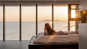 A bedroom with a large window overlooking the sea, a bed, and a nightstand. - Uljin French Paper Pension (Uljin)