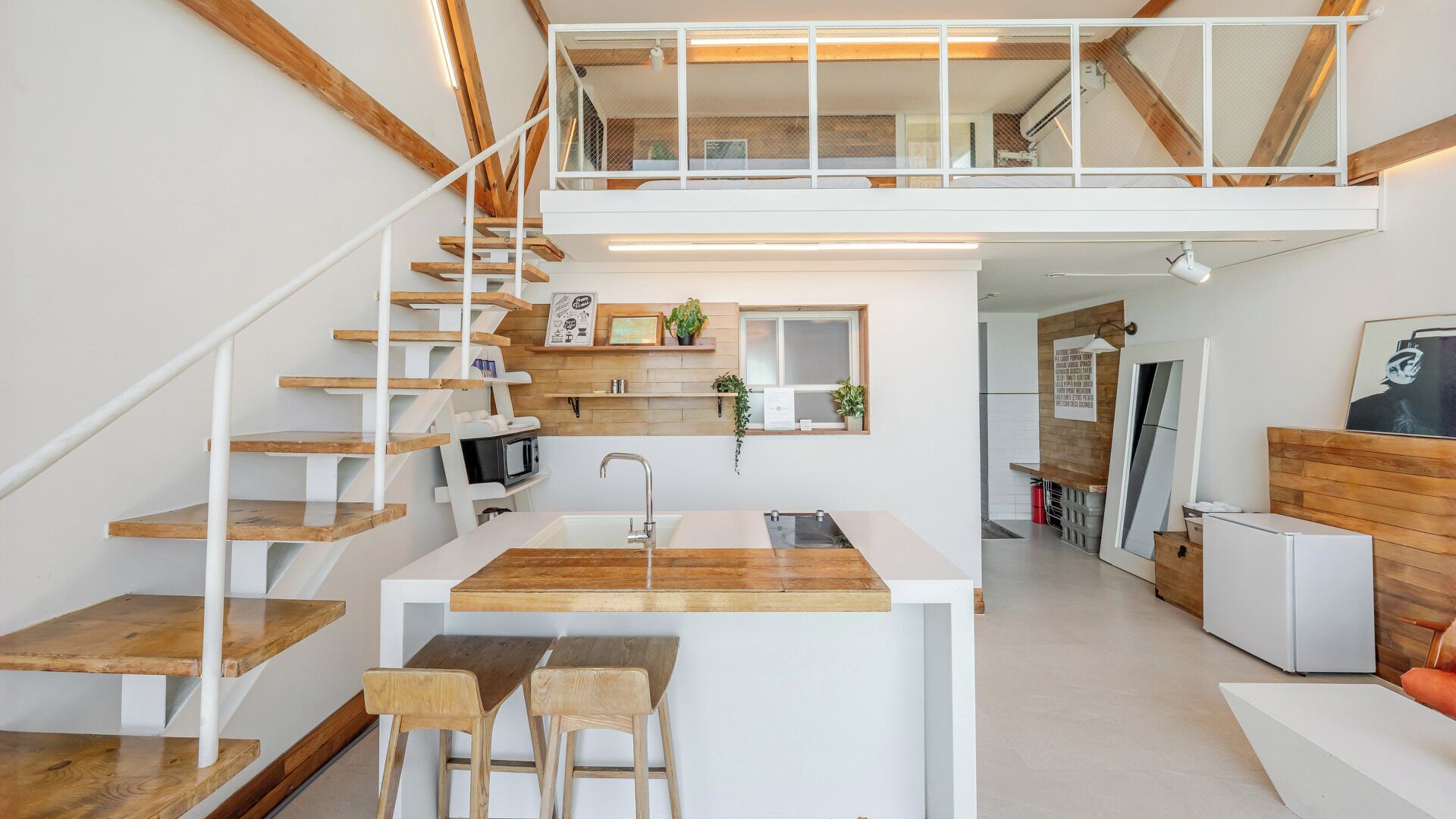 Una cocina moderna con una isla central, una escalera de madera y un altillo con dormitorio.