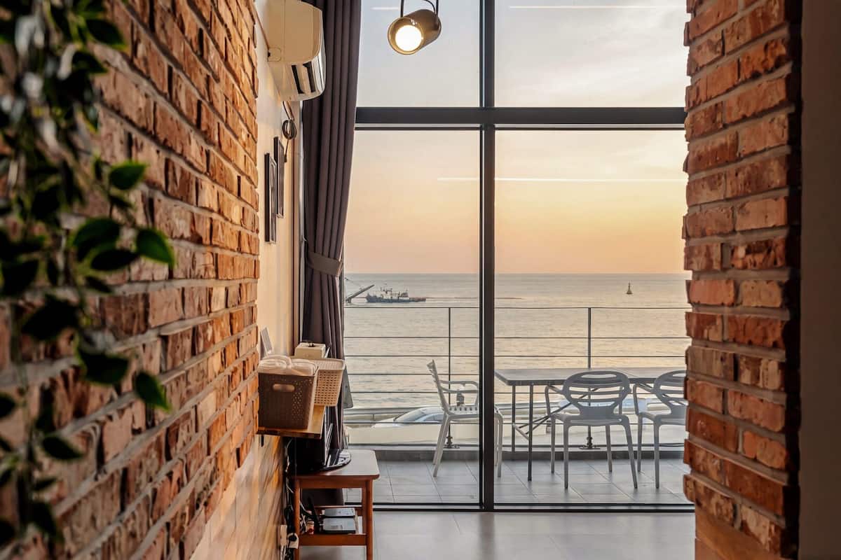 Una habitación con un ventanal grande que da al mar, una pared de ladrillo y una mesa con sillas.