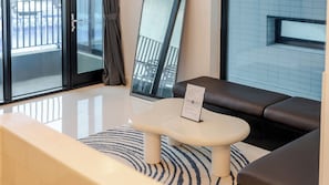 Una sala moderna con un sofá, una mesita con un menú, un tapete a rayas y ventanas grandes con vistas a un balcón.
