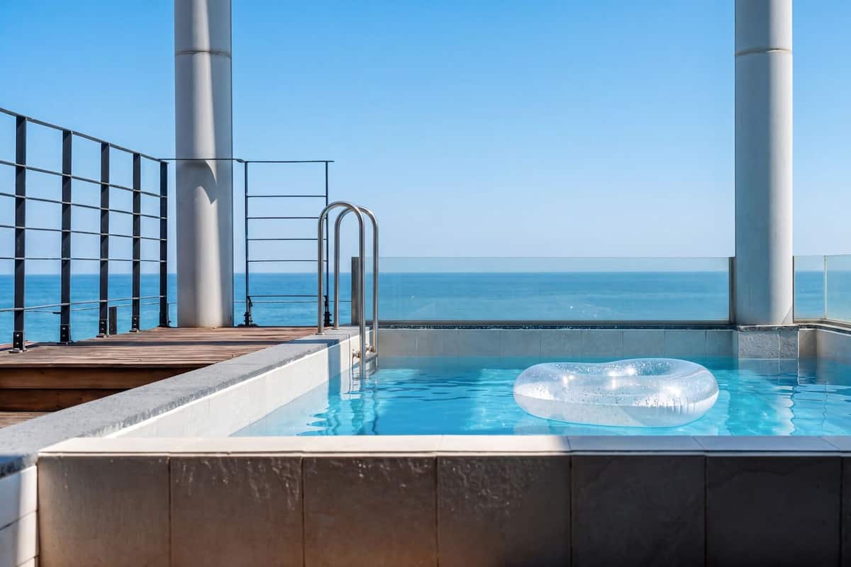 Una piscina con vista despejada al océano, una escalera metálica y una terraza de madera.