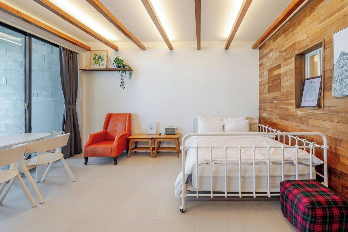 Un dormitorio con cama, escritorio, silla, mesita de noche y ventana.