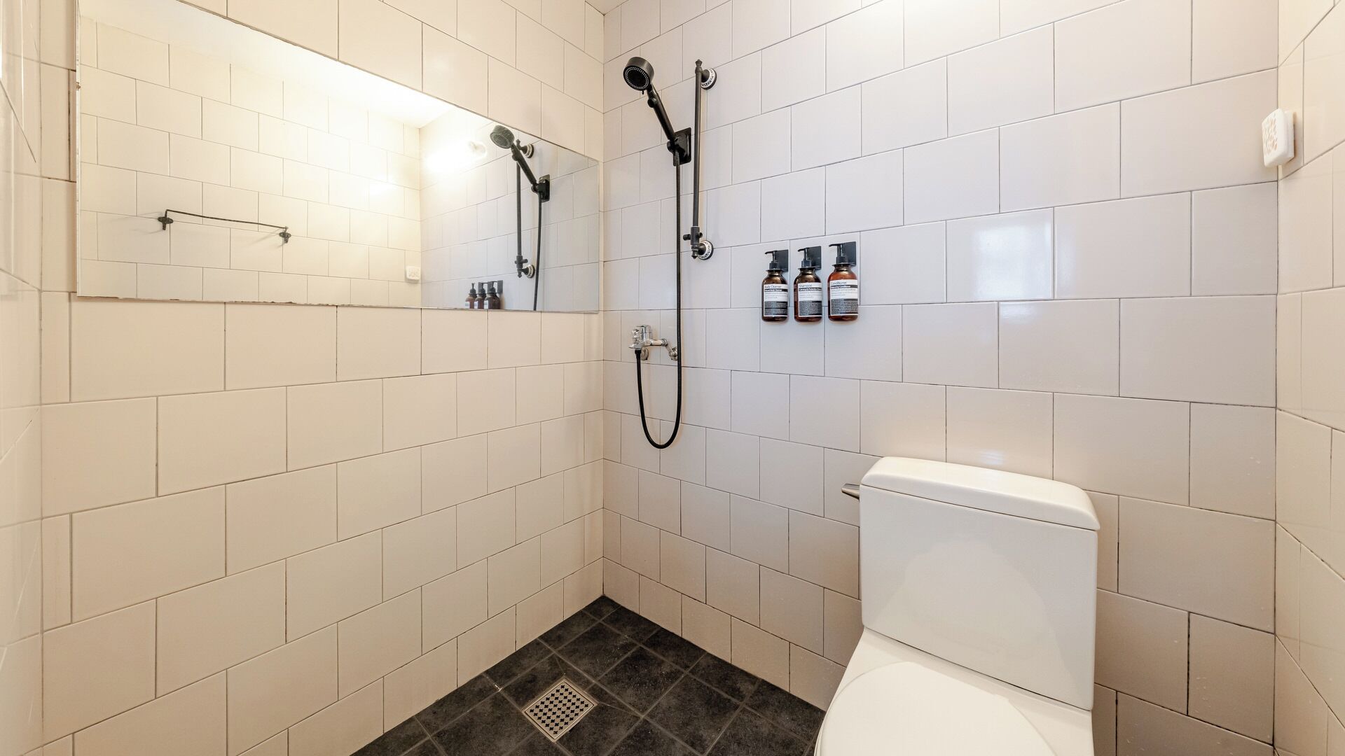 Un baño con azulejos blancos, ducha, inodoro y espejo.