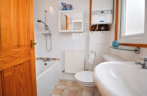 Et badeværelse med badekar, toilet, håndvask og en glashylde.