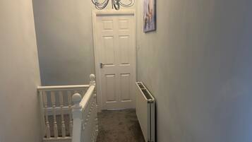 A hallway with a white door, a radiator, and a chandelier.