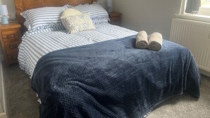 Ein ordentlich bezogenes Bett mit gestreifter Bettwäsche, einer blauen Decke und aufgerollten Handtüchern.