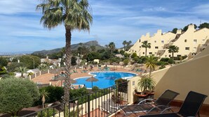 Ein Poolbereich mit Liegestühlen, einer Palme und Blick auf ein Gebirge.