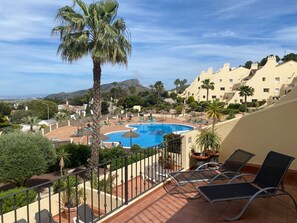 Ein Poolbereich mit Liegestühlen, einer Palme und Blick auf ein Gebirge.