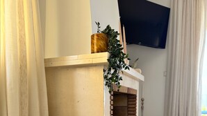 Ein Wohnzimmer mit Kamin, einem an der Wand befestigten Fernseher und einem Fenster mit Vorhängen.