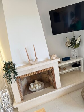 Ein modernes Wohnzimmer mit Kamin, einem flachbildfernseher an der Wand und einem weißen Konsolentisch mit Dekoration.