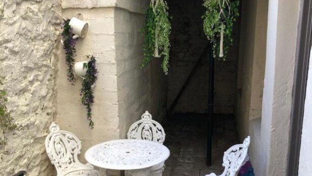 Een terras met een witte tafel en stoelen, hangplanten en een stenen muur.