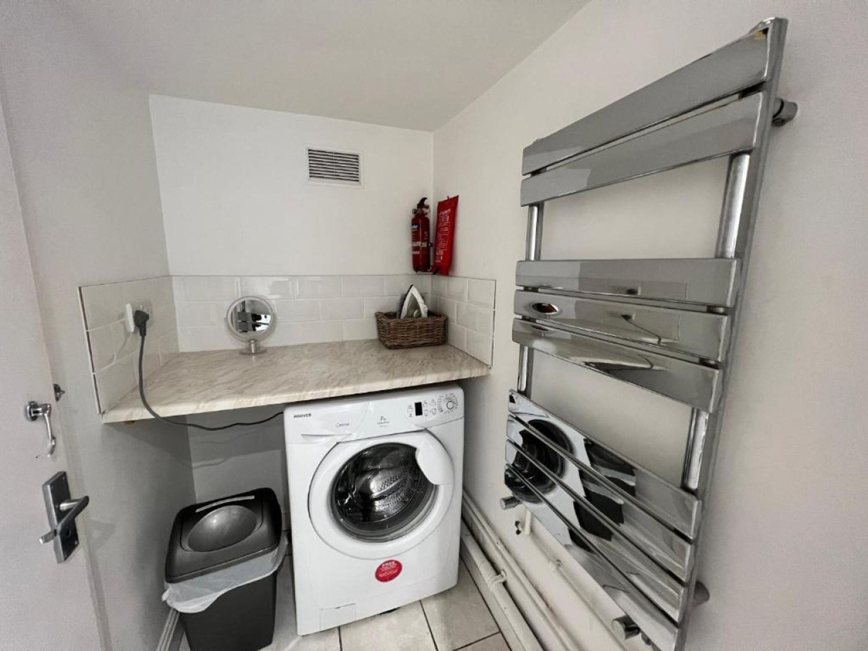 A compact laundry room with a washing machine, a drying rack, and a small shelf with a basket.