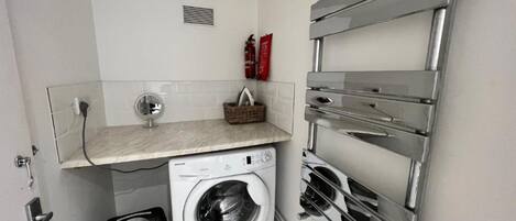 A compact laundry room with a washing machine, a drying rack, and a small shelf with a basket.