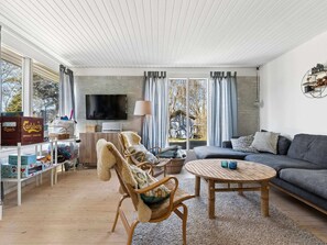 A living room with a sofa, armchair, coffee table, TV, and a window with curtains. - 4 Star Holiday Home in Gilleleje (Gilleleje)