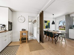 A modern kitchen with white cabinets, a wooden table, and a dining area with green chairs. - 4 Star Holiday Home in Gilleleje (Gilleleje)