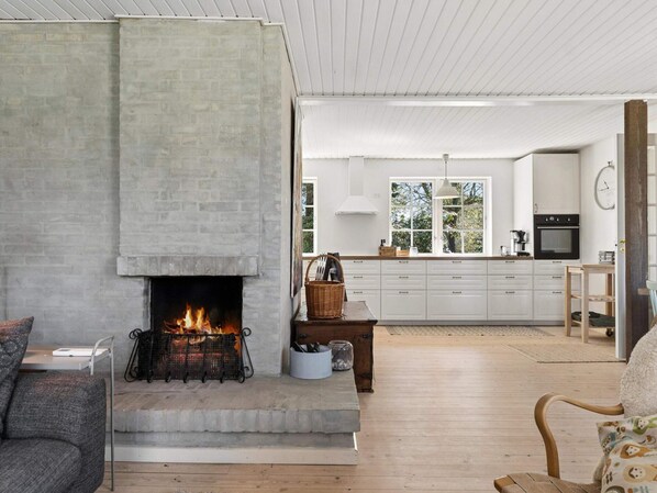A modern living room with a fireplace, a kitchen with white cabinets, and a dining area. - 4 Star Holiday Home in Gilleleje (Gilleleje)