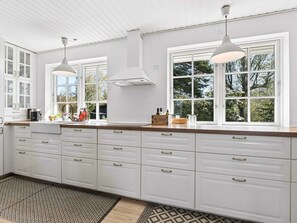 A kitchen with white cabinetry, a large window, and pendant lighting. - 4 Star Holiday Home in Gilleleje (Gilleleje)