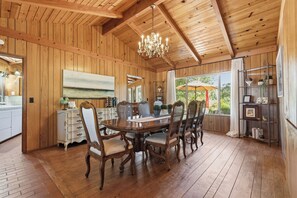Una habitación con paneles de madera, una mesa de comedor, sillas, una araña y vistas amplias a través de grandes ventanales.