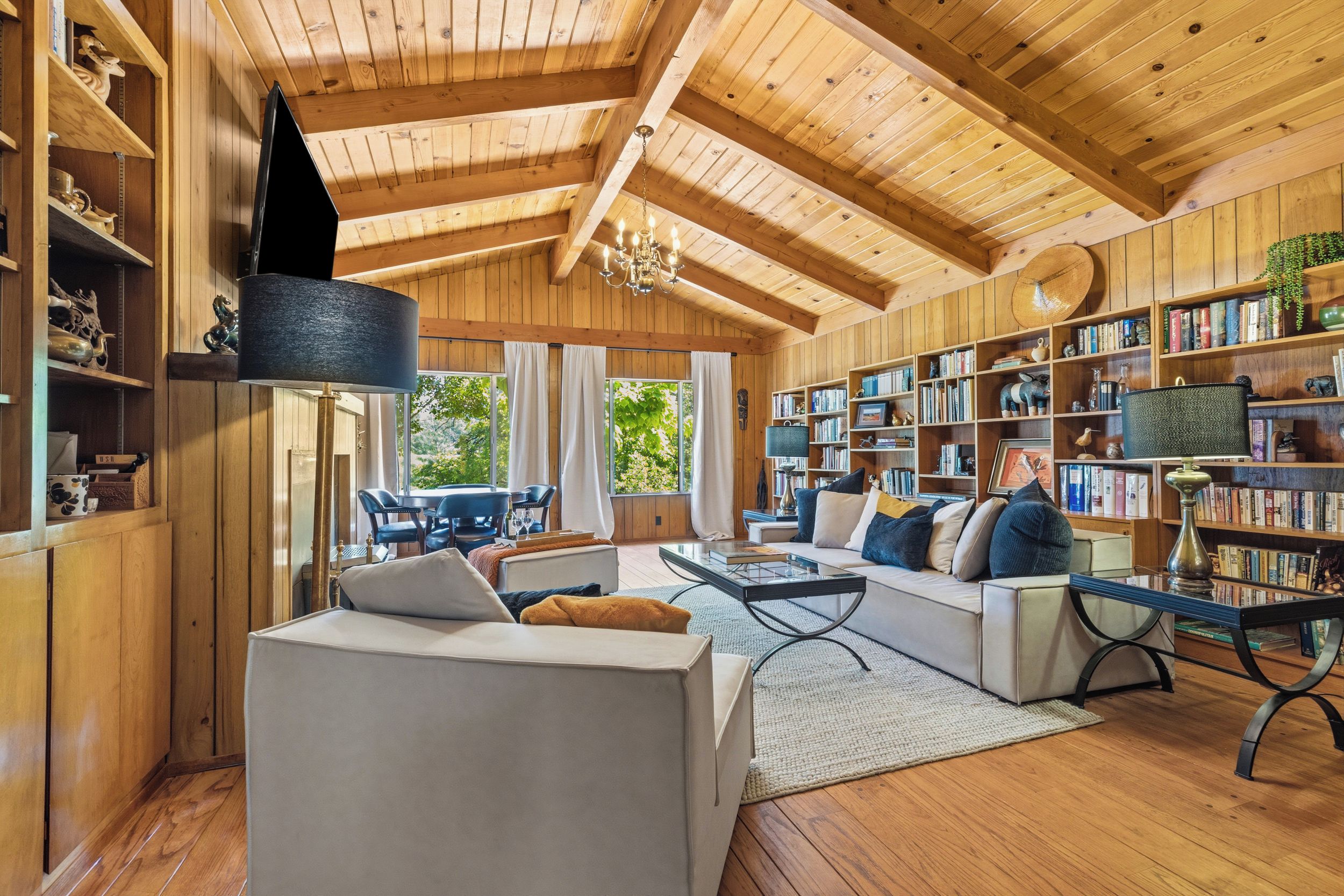 A spacious living room with a high ceiling, wooden beams, a large bookshelf, and a cozy seating area with a sofa and chairs.