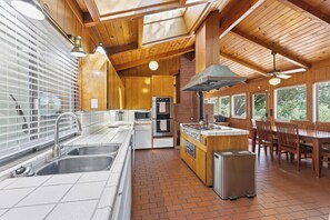 A modern kitchen with a central island, stainless steel appliances, and a dining area with wooden furniture. - Private Wine Country Escape With Sweeping Valley Views, Hot Tub, Apple Hill (Placerville)