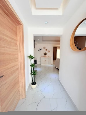 A hallway with a wooden door, a potted plant, a white cabinet, and a round mirror on the wall. - 2-level Villa With Private Pool 3BR (Punta Cana)