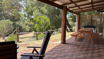 Un patio al aire libre con una mesa y sillas de madera, techo cubierto y vista a un paisaje natural.