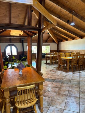 A spacious dining area with wooden tables and chairs, a fireplace, and a view of the outdoors. - Augusta Sheoak Chalets (Augusta)