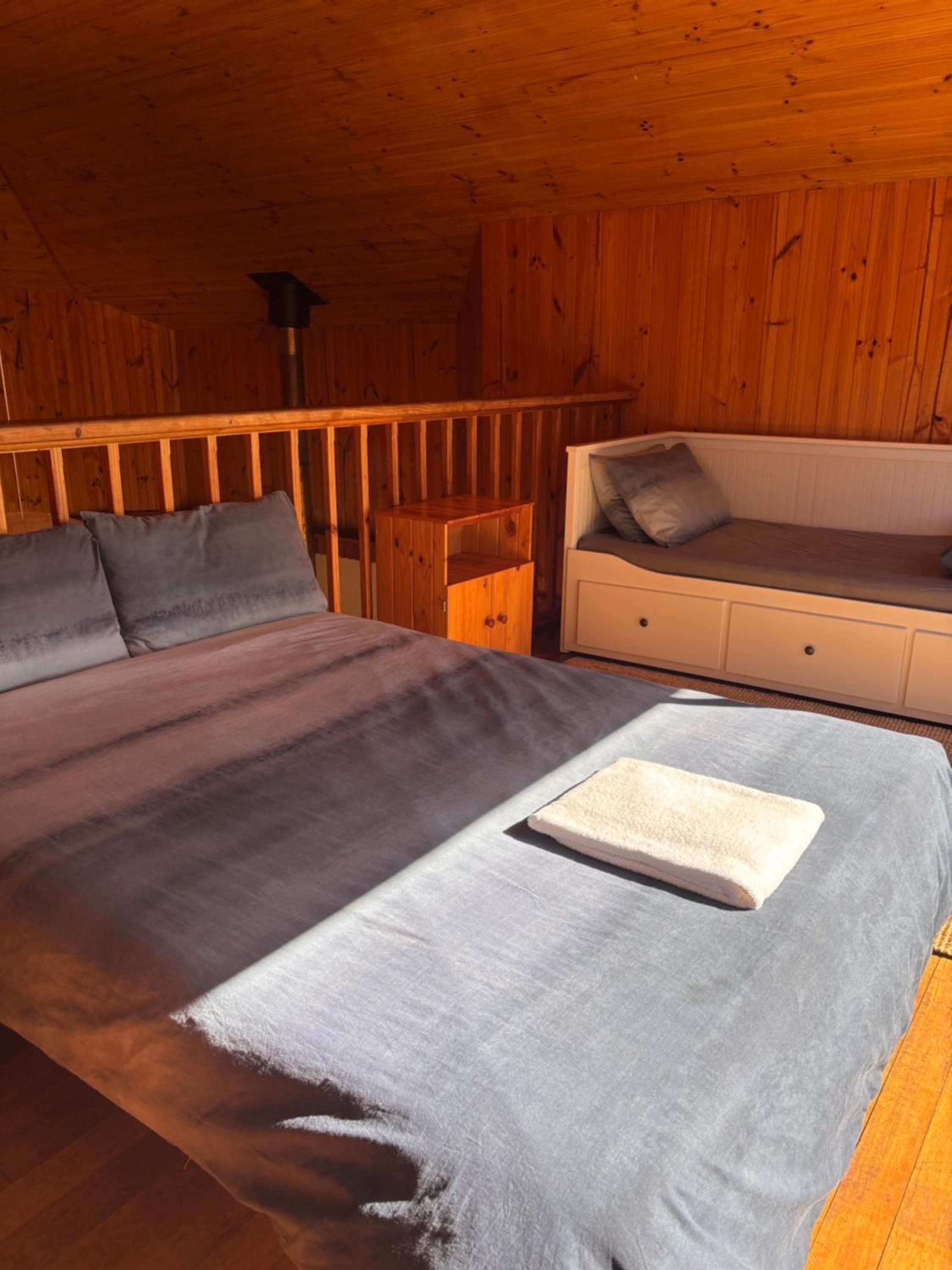Ein Zimmer in einer Holzhütte mit einem Bett, einem kleinen weißen Schminktisch und einer Bank mit Kissen.