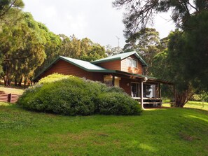 A wooden house with a green roof, surrounded by lush greenery and trees. - Augusta Sheoak Chalets (Augusta)