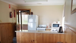 A compact living space with a kitchenette, a brown leather sofa, and a wooden floor. - Augusta Sheoak Chalets (Augusta)