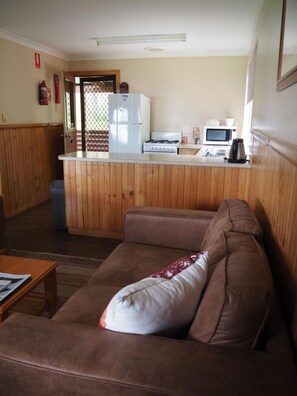 Un espacio habitable compacto con kitchenette, un sofá de cuero marrón y piso de madera.