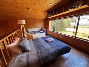 A wooden cabin room with a bed, a nightstand, a window, and a view of the outdoors. - Augusta Sheoak Chalets (Augusta)