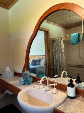 A bathroom with a large mirror, a sink, a shower, and a bed visible in the reflection. - Augusta Sheoak Chalets (Augusta)