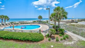 Un espace piscine avec vue sur la plage, entouré de palmiers et d’une clôture.