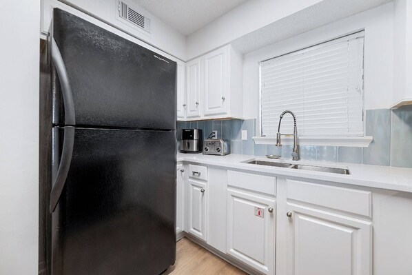 A compact kitchen with a black refrigerator, white cabinets, a microwave, and a sink with a faucet. - Seaside Beach and Racquet 5617 | BeachFront + Pool (Orange Beach)