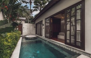 A swimming pool with a hot tub, surrounded by lush greenery and a modern house with large windows.