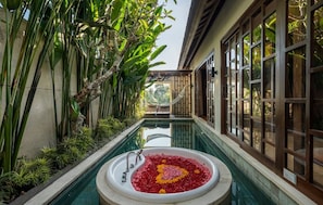 A pool with a flower arrangement, surrounded by tropical plants and large windows.