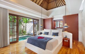 A spacious bedroom with a large bed, a small sitting area, a pool view, and a wooden ceiling. - asvara villa (Ubud)