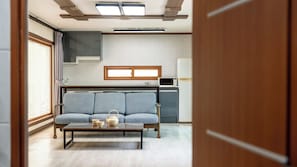 A compact living space with a sofa, a coffee table, a microwave, and a small kitchen area.