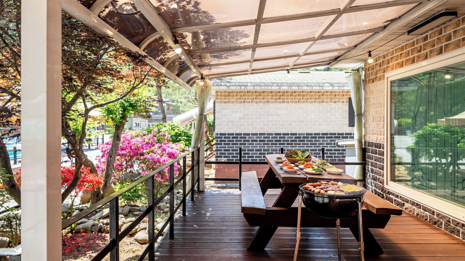 An outdoor dining area with a grill, wooden benches, and a view of a brick building.
