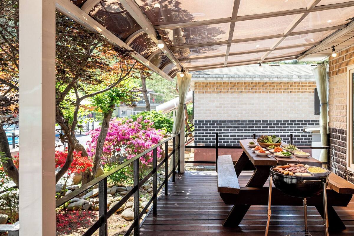 Un espacio para comer al aire libre con una parrilla, bancos de madera y vista a un edificio de ladrillo.