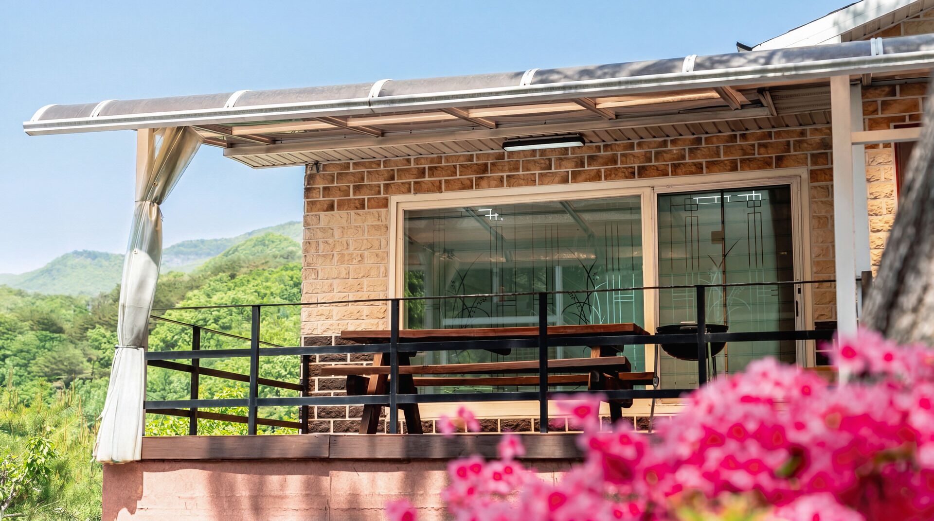 A balcony with a wooden bench, a glass door, and a view of green hills.