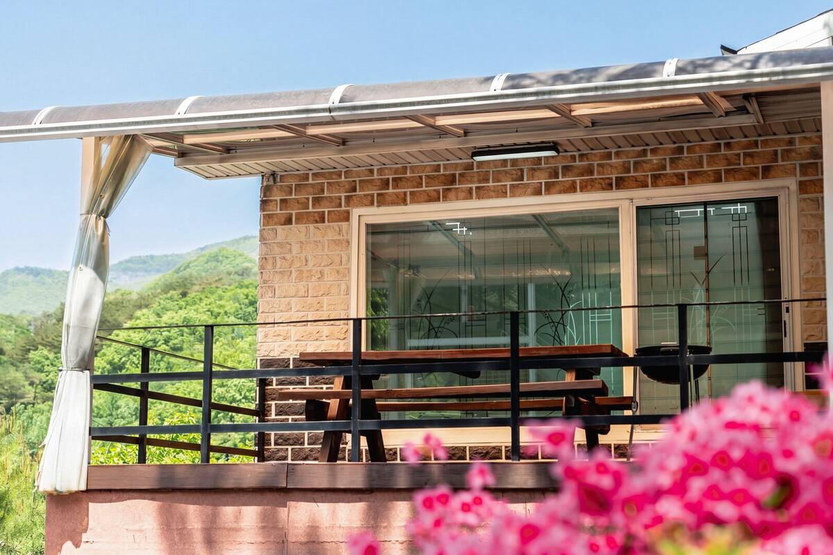 Un balcón con banca de madera, puerta de cristal y vistas a colinas verdes.