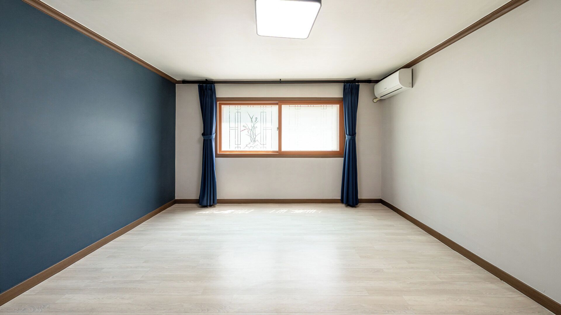 Een kamer met een groot raam, houten vloeren en blauwe wanden.