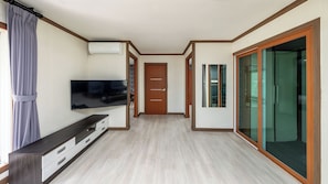 A hotel room with a flat-screen TV, a wooden cabinet, a sliding glass door, and a door with a handle.