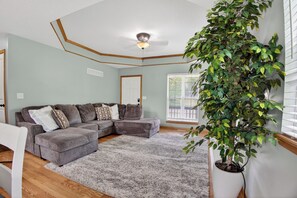 Uma sala de estar com sofá modular, tapete felpudo, ventilador de teto e planta em vaso.