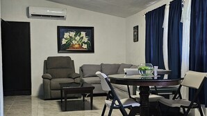 A living room with a sofa, armchairs, a dining table, and a ceiling fan.