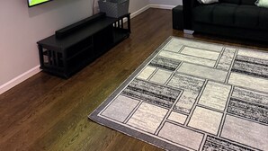 A living room with a flat-screen TV mounted on the wall, a black sofa with a cushion, a patterned rug, and a wooden floor. - Modern 3BR Jersey City Retreat Near NYC & FIFA (Jersey City)