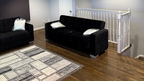 A living room with two black sofas, a patterned rug, wooden flooring, a white door, and a white railing. - Modern 3BR Jersey City Retreat Near NYC & FIFA (Jersey City)