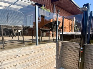 A wooden deck with a glass enclosure, a barbecue grill, and outdoor furniture. - 5 Star Holiday Home in Frederikshavn (Frederikshavn)